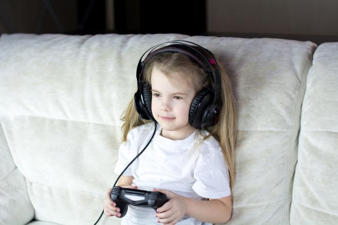 Una niña sentada en un sofá jugando videojuegos con auriculares puestos