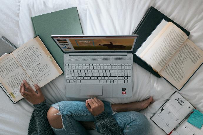 Vista superior de una persona sentada en su cama, estudiando, con una laptop y varios libros