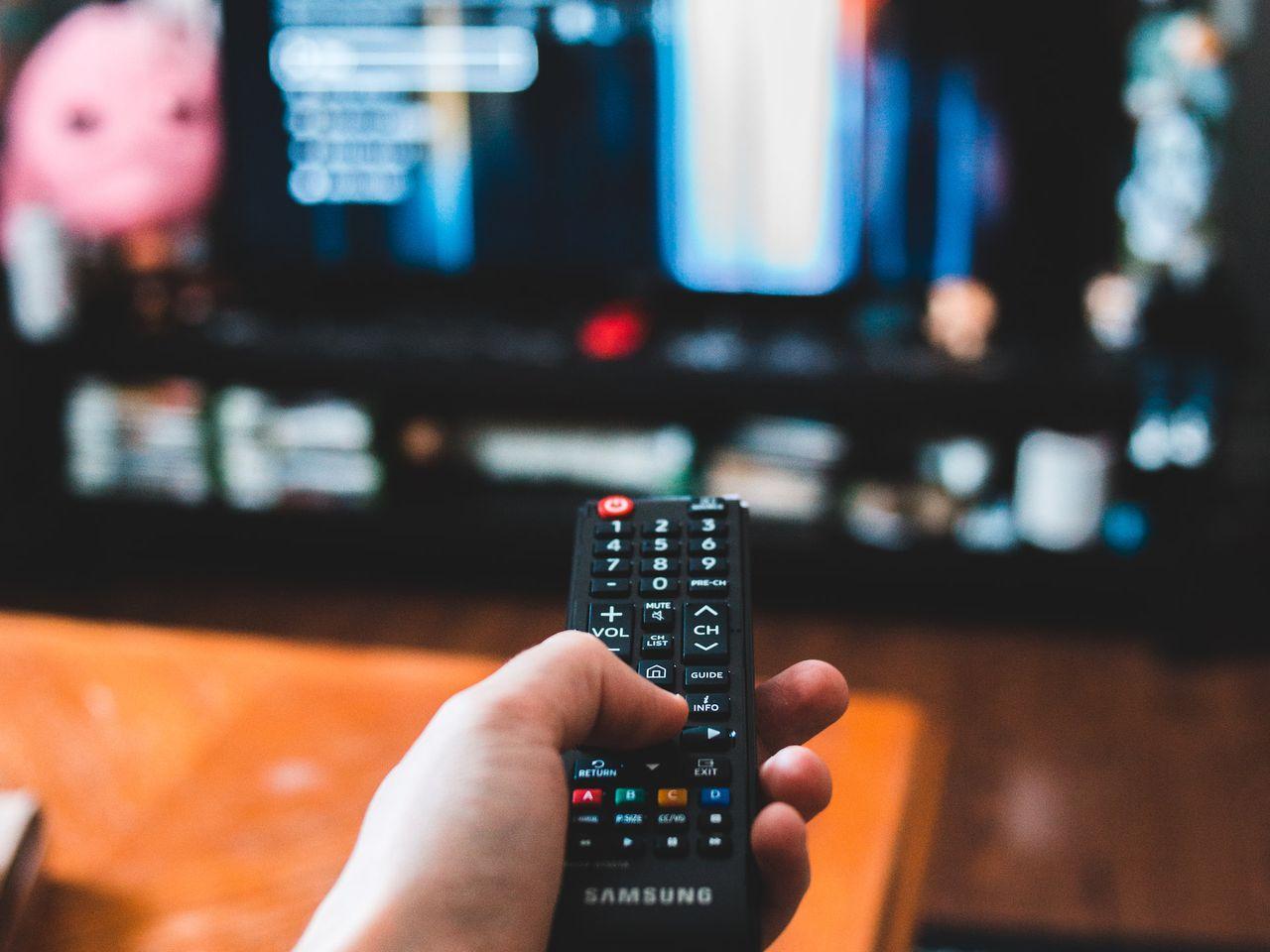 Mano sosteniendo un control remoto frente a una TV