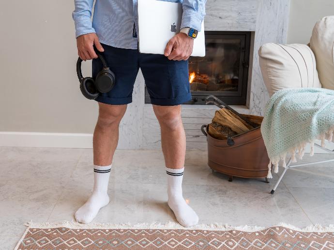 Un hombre vistiendo shorts y calcetines sin zapatos, sosteniendo una laptopt y diademas