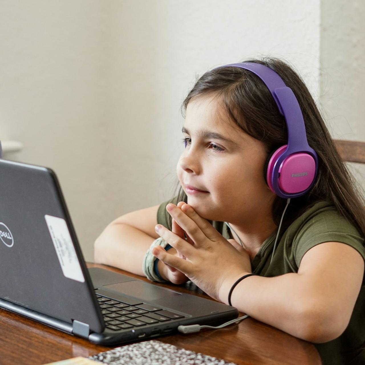 a little girl sitting at a table with a laptop